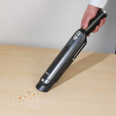 Close-up of a person using the Beldray cordless handheld vacuum to clean crumbs from a wooden surface.