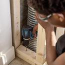Worker using DXPULSE cordless drill to drive a screw into wooden stud framing near exposed conduit, construction DIY installation scene with power tool in action.
