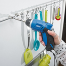 Close-up of cordless screwdriver tightening a wall-mounted rail with kitchen utensils hanging on hooks.