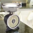 Mechanical kitchen scale with metal bowl placed on a kitchen countertop.