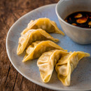 Close-up of dumplings served on a grey speckled plate with a small bowl of dipping sauce on a wooden surface.