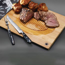 Wooden carving board with roast beef and Yorkshire puddings, accompanied by carving knife and fork.
