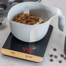 Mixing bowl with ingredients placed on digital kitchen scale showing weight in red LED display.