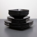 Neatly stacked matt black square plates with bowls on top against a dark surface.