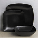 Close-up of matt black square dinner plate, side plate and bowl arranged together on a table.