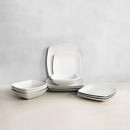 Matt white square plates and bowls stacked and displayed on a tabletop against a neutral backdrop.