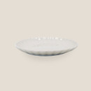 Shallow cream ceramic plate with scalloped edge, side view.