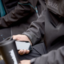 Close-up of jacket sleeve with Makita logo and person holding a smartphone