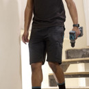 Tradesperson wearing black Makita work shorts holding a cordless drill indoors on a construction site