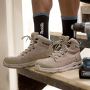 Close-up of black Makita work socks worn with beige safety boots on a construction site, showing ribbed fit and logo detail