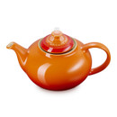 Close-up side view of orange glazed teapot with curved spout and handle