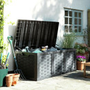 Large black rattan-effect garden storage box with lid open, holding tools and accessories on a patio