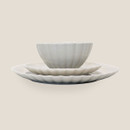 White stoneware dinner set with scalloped edges, including a bowl, side plate and dinner plate stacked together on a light background.