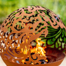 Close-up of the laser-cut dragon motif on a rust-effect steel fire globe, with flames visible through the decorative metalwork.
