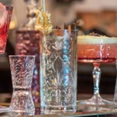 Decorative highball glass displayed alongside cocktail glasses and mixed drinks, highlighting the elegant embossed pattern and versatile drinkware style.
