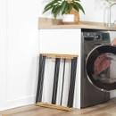 Folded Beldray bamboo clothes airer stored neatly beside a washing machine, demonstrating the compact space-saving design.