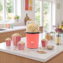 Giles & Posner popcorn maker filled with freshly popped popcorn, displayed on a kitchen island with striped popcorn tubs and snack ingredients.