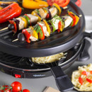 Close-up of vegetable skewers cooking on the raclette grill, highlighting the ridged non-stick grilling surface.