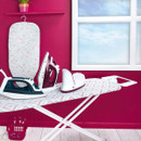 Kleeneze ironing board set up in a laundry room with a steam generator iron and laundry basket, ready for ironing.