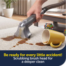Handheld cleaning nozzle scrubbing and extracting a fresh spill from carpet, ideal for tackling everyday household accidents.