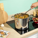 Large Russell Hobbs stainless steel stockpot cooking a vegetable and bean stew on an induction hob, with a serving spoon in use.