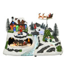 Festive tabletop Christmas village featuring a snow-covered house, rotating sleigh ride, illuminated waterfall, winter characters and frosted pine trees with colourful LED lights.