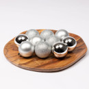 Collection of silver Christmas baubles in mixed finishes arranged on a wooden tray, including shiny mirrored, matte and glitter ornament designs.