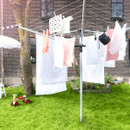 Brabantia rotary washing line in use outdoors with towels, clothing and linens hanging across multiple drying lines.