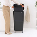 Person accessing the upper compartment of a Brabantia SortUp dual recycling bin with the lid open and inner bucket visible.