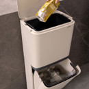 Brabantia SortUp dual recycling bin with the lid open while recyclable packaging is placed into the upper compartment and bottles stored below.