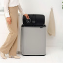 Brabantia Touch Bin 60L with the lid open while a user disposes of a plastic container, demonstrating easy touch-open operation.