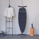 Brabantia Steam & Iron Board in upright position displayed in a modern interior with clothing hanging nearby.