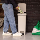 Person disposing of packaging waste into the open soft beige Brabantia StepUp pedal bin in a modern kitchen.
