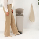 Person opening the soft beige Brabantia StepUp pedal bin using the foot pedal, demonstrating hands-free operation.