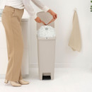 Person securing a bin liner inside the open soft beige Brabantia StepUp pedal bin.