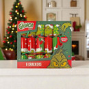 The Grinch Christmas cracker set featuring six festive crackers in a themed presentation box, displayed on a table with a decorated Christmas tree and cosy holiday background.