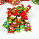 Pile of The Grinch Christmas crackers featuring bright red and green festive patterns, ribbon ties and character artwork, displayed on a white surface.