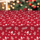 Red Christmas wipe clean tablecloth displayed on a table, decorated with white robin, berry branch, snowflake and festive foliage motifs, with a Christmas tree softly blurred in the background.