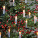 Close-up of warm white candle-style Christmas tree lights clipped among green branches and red berry garlands.