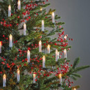 Christmas tree decorated with warm white candle clip lights and red berry garlands, creating a traditional festive display.