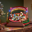 Animated Christmas fairground ride decoration with colourful LED lights, spinning teacup-style seats, festive figures, and a "Merry Christmas" sign, displayed on a tabletop.