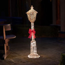 Illuminated Christmas lamp post decoration with warm white LED lights and a festive red bow, displayed outdoors to create a welcoming holiday entrance.
