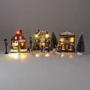 Illuminated Christmas village scene featuring a bookshop, gift shop and theatre with glowing LED lights, festive figurines, snow-covered trees and traditional street lamps for seasonal home décor.