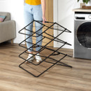 Black collapsible clothes drying rack being folded down by hand, showing the expandable multi-level design for compact storage.