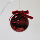 Close-up of a glossy red glass Christmas bauble finished with a red velvet bow and gold hanging loop.