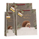 Coordinated Christmas gift bag set featuring a snowy hedgehog illustration, festive foliage border, gold foil “Christmas Wishes” lettering, matching gift tag and red rope handles.