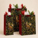 Three Christmas gift bags in assorted sizes featuring a stag, woodland animals, ornate gold foliage, red sides and festive tissue paper.