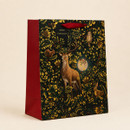 Christmas gift bag featuring a stag and woodland animals among ornate gold foliage, with red sides and a red ribbon handle.