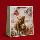 Christmas gift bag featuring a Highland cow and calf in a snowy woodland scene with holly, red berries and a red rope handle.