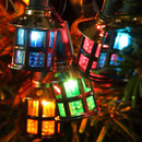Close-up of colourful miniature lantern LED Christmas lights with textured panels and warm illumination, displayed on a Christmas tree with green pine needles.
